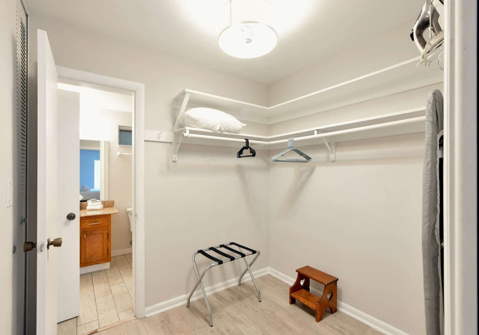 Open closet with shelves, hangers, bench, and bathroom view