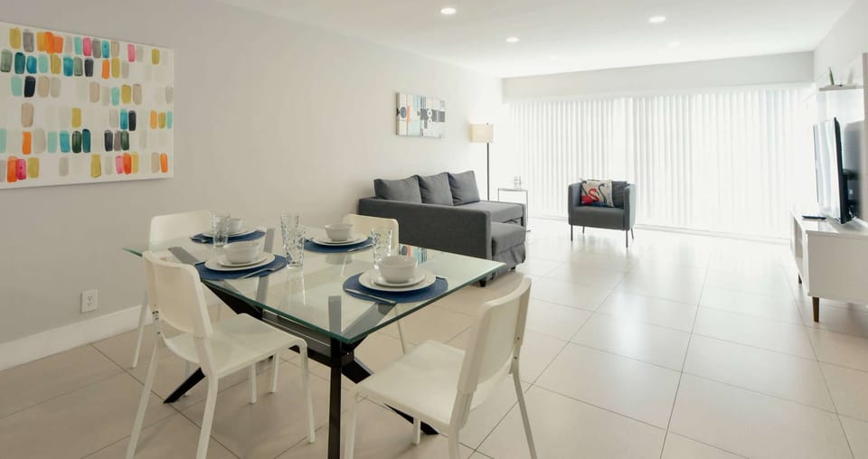 Bright dining and living area with sofa, chair, TV, and windows