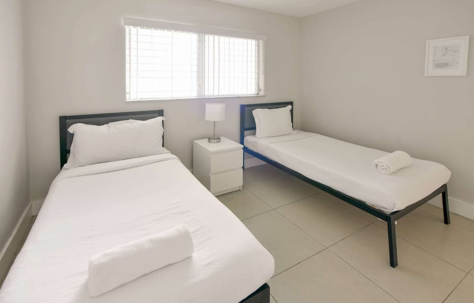 Twin bedroom with two beds, side table, lamp, and window