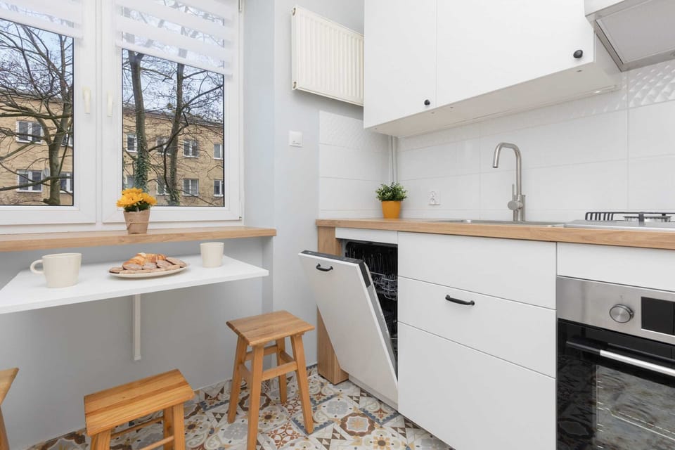 Bright and airy kitchen with white cabinets, bar stools, and a view of the greenery outside the window.






