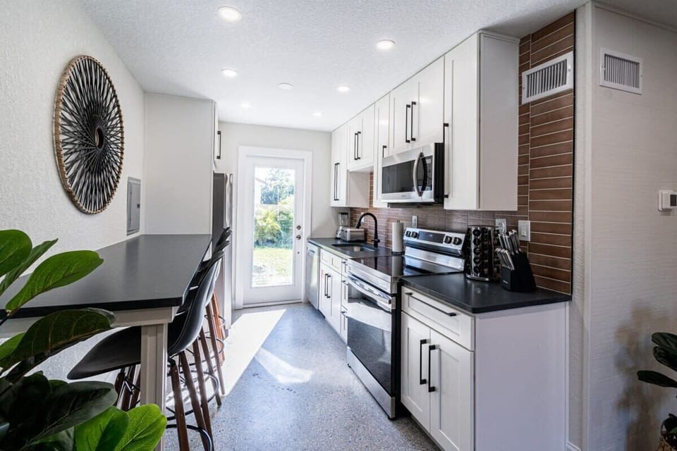 Modern kitchen with white cabinetry, black countertops, and a breakfast bar with seating.