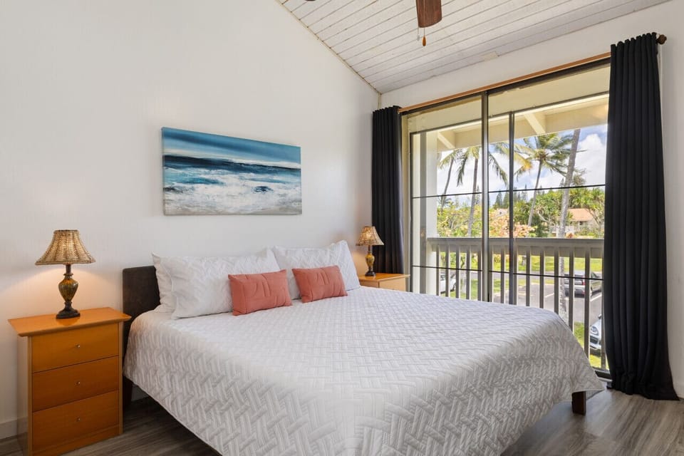 Bright bedroom w/ soft linens & views framed by palm-lined windows.