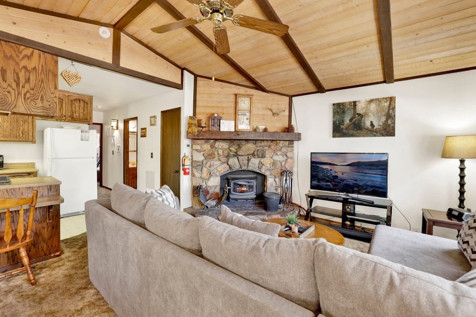 Cozy mountain living room with a stone fireplace, comfy seating, and smart TV—perfect for relaxing evenings, movie nights, and warm cabin vibes after outdoor adventures.