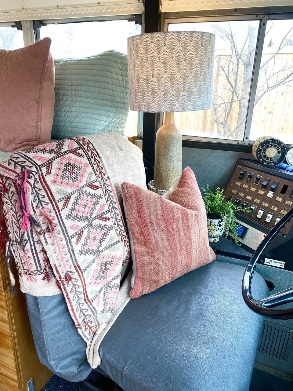 Curated textiles resting on the original driver's seat, vintage dash controls still intact. The Riviere Skoolie on Lake Granbury kept the character where it counts. Unique skoolie rental near Fort Worth and Granbury, TX.