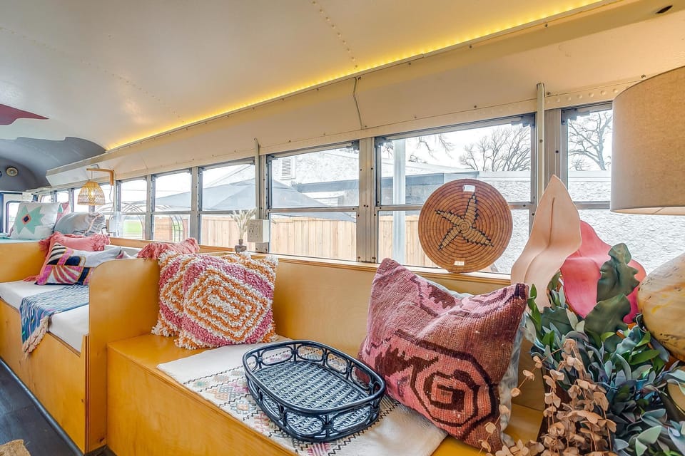 Layered textiles, woven wall art, and warm ambient lighting along the window bench inside Hope. Every inch of The Riviere Skoolie on Lake Granbury was curated. Unique converted school bus rental near Fort Worth, TX.