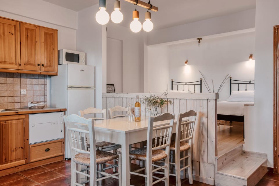 Apartment kitchen, dining area, and two single beds on wooden level, bathroom.