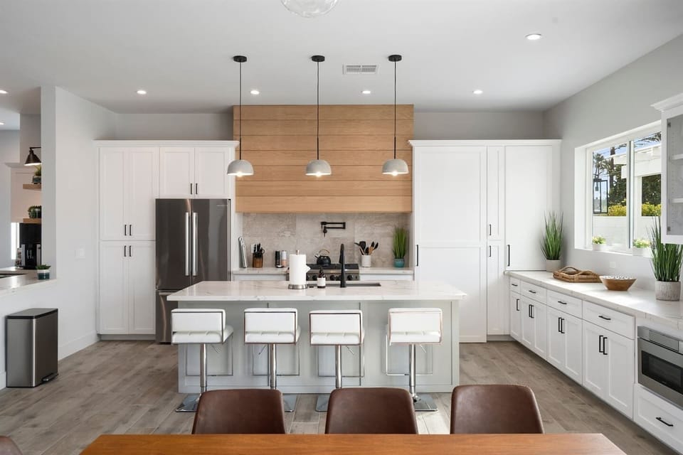 Fully equipped kitchen with gas range, fridge, microwave, and a stylish island with seating. The separate coffee area and wine cooler make it perfect for relaxing. Elegant white theme with marble and wood accents.
