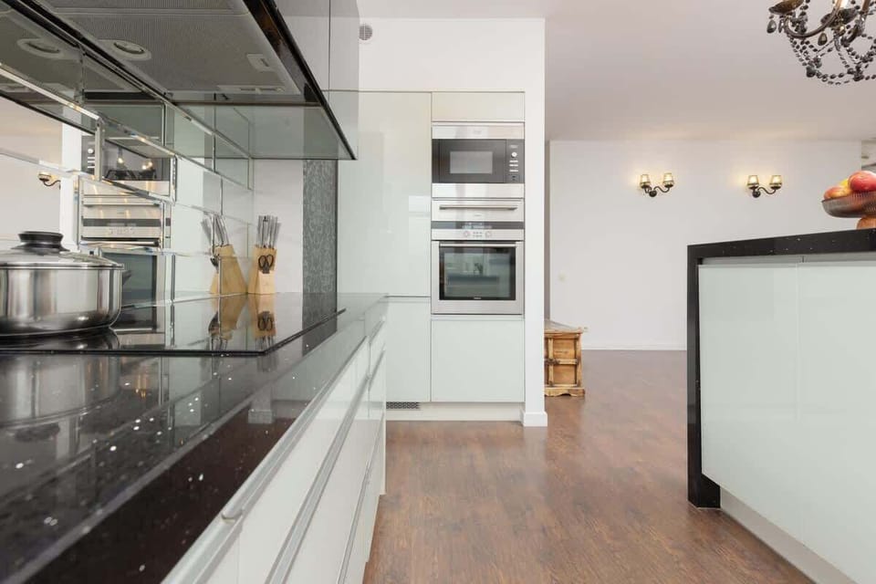 A sleek kitchen with a black backsplash, glossy white cabinets, and stainless steel appliances.
