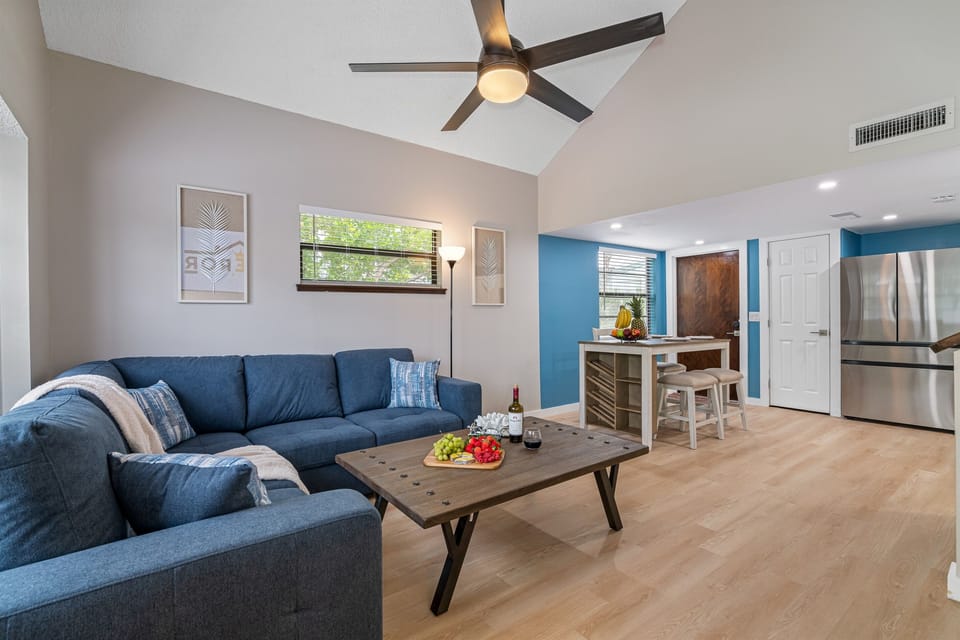 Step into a world of refined sophistication where a soothing color palette, a plush blue sofa, expansive windows, and warm wooden floors come together to create an inviting haven.