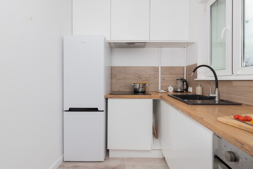 A modern white kitchen fitted with a fridge, stove, and wooden countertops.
