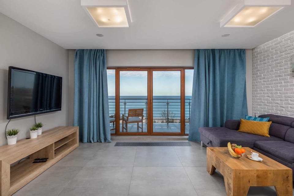 A cozy living room with a gray couch and blue curtains, featuring a wooden coffee table and a view of a balcony, letting in plenty of natural light.