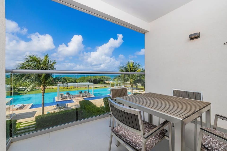 Stunning balcony where you can enjoy meals with views of the sparkling pool, lush palms, and turquoise ocean beyond—your perfect spot to relax and soak in paradise.
