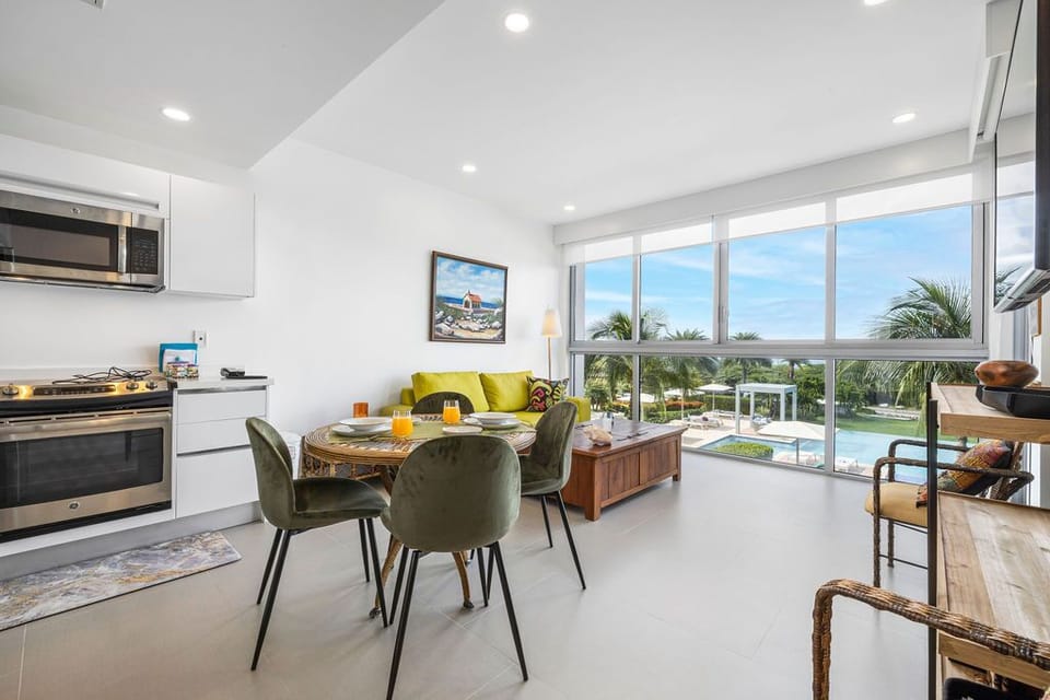 Step into your bright, airy retreat where palm trees frame the poolside view. Enjoy meals at your cozy dining table, unwind on the chartreuse sofa, and whip up favorites in your modern kitchen.