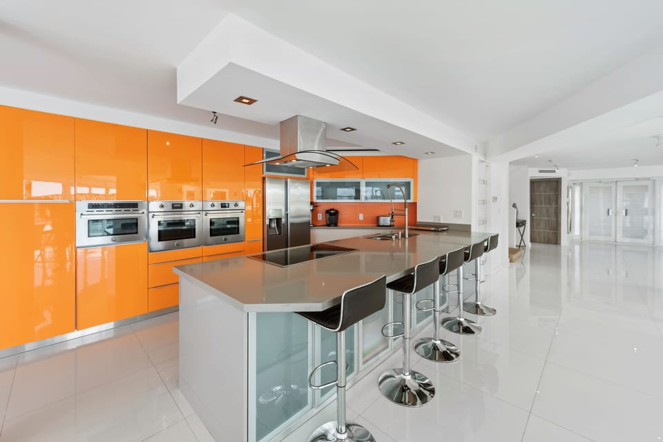 Gourmet kitchen centerpiece featuring a large island with seating for six, custom high-gloss cabinetry, stainless steel appliances, built-in double ovens, quartz countertops, and an open layout designed for cooking and entertaining.