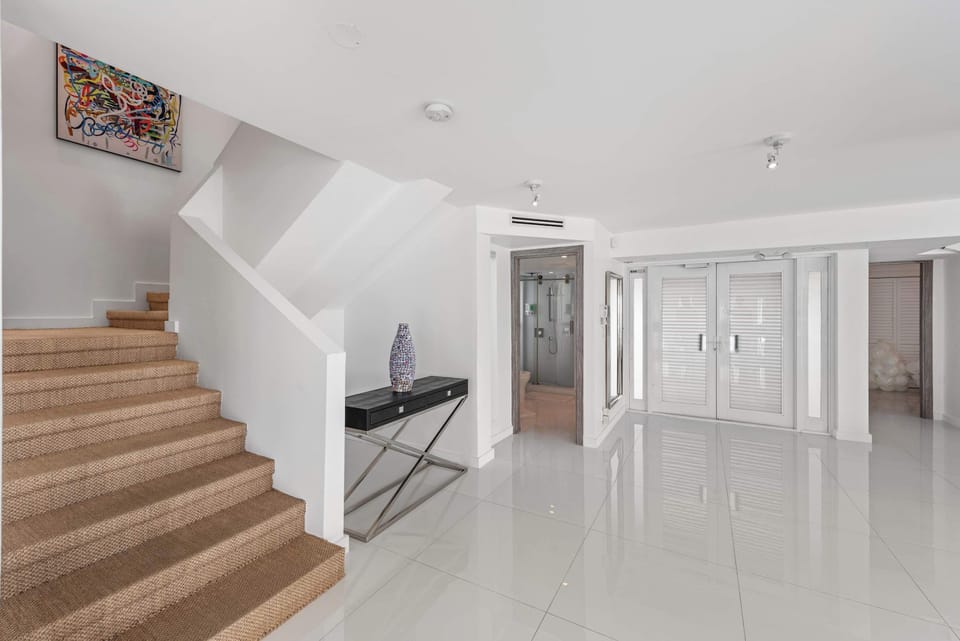 Spacious entry level featuring a carpeted staircase, glossy tile flooring, built-in storage closets, elevator access, contemporary furnishings, and convenient circulation to guest rooms and shared living areas.