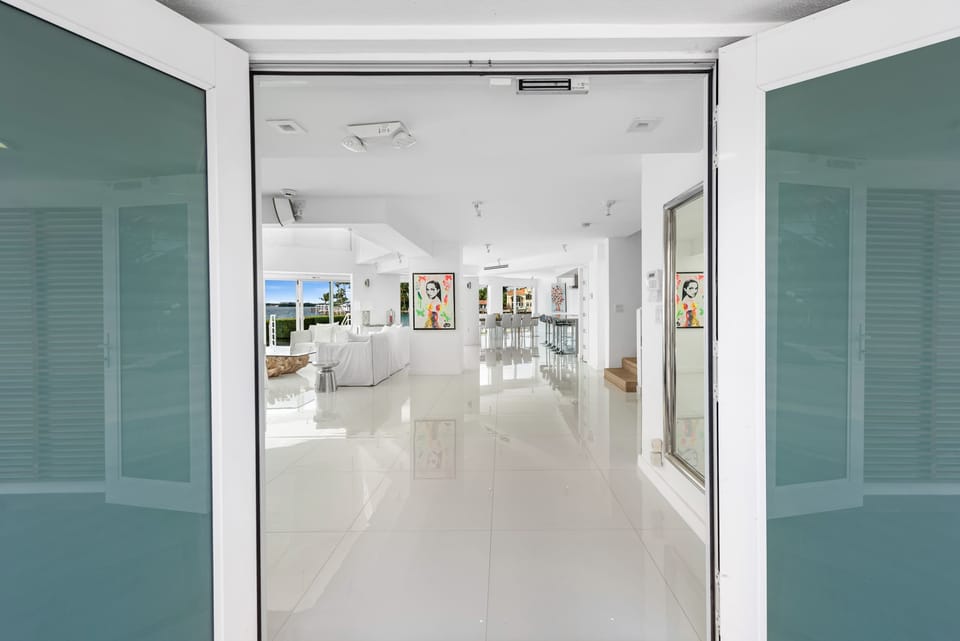 Wide entryway view showcasing the home's open-concept layout, glossy tile flooring, abundant natural light, modern interior design, and direct sightlines to the living, dining, and waterfront gathering spaces.
