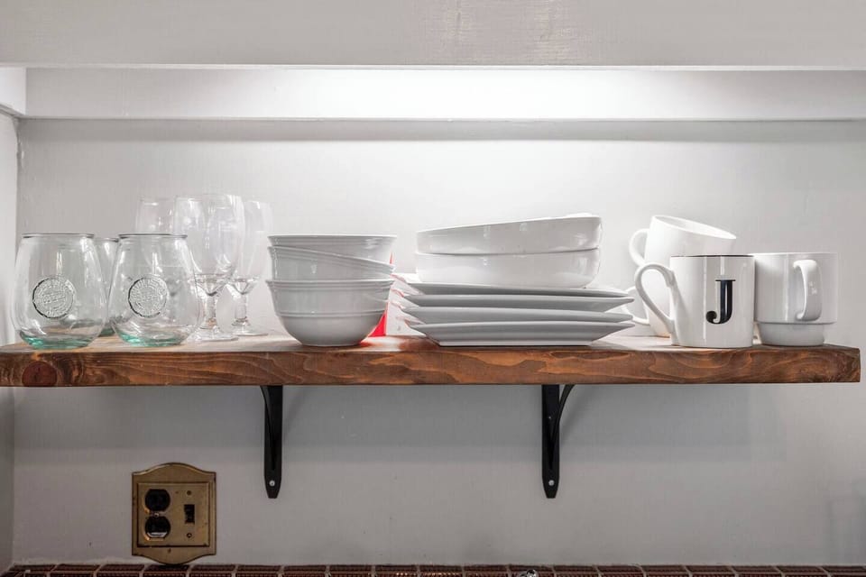 Plates and cups on shelf above kitchen sink.