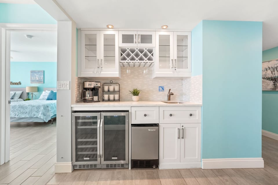 Your elegant kitchenette features white cabinetry, wine cooler, and coastal charm with soothing blue accents throughout your beachside retreat.