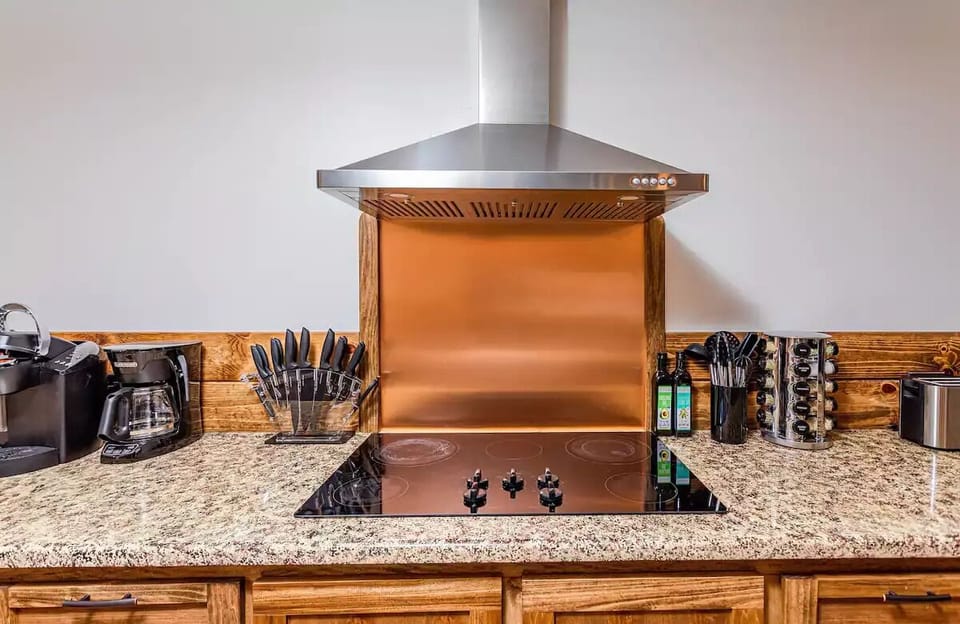 Cooktop with copper backsplash, range hood, and small appliances