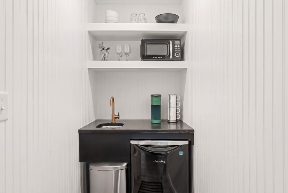 In-suite wet bar — Keurig, mini-fridge, microwave, sink, and dishware. Self-sufficient without leaving the suite.