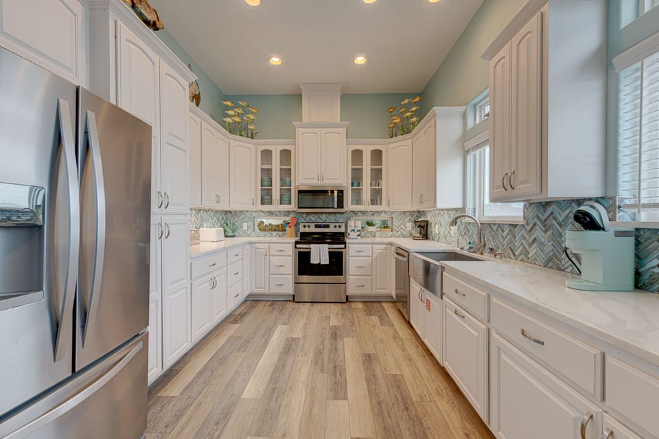 Your dream kitchen awaits with sparkling white cabinets, stainless steel appliances, and a stunning herringbone backsplash that catches the coastal light beautifully.