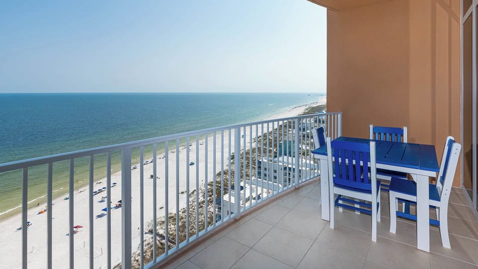 Step onto the balcony, sit at the blue table, and listen to gulf surf while watching the beachfront below