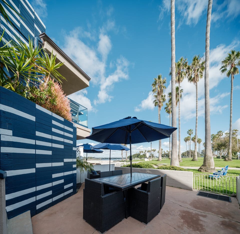 This expansive outdoor area is ideal for gatherings, featuring spacious dark brown rattan dining tables with umbrellas, perfect for a BBQ.