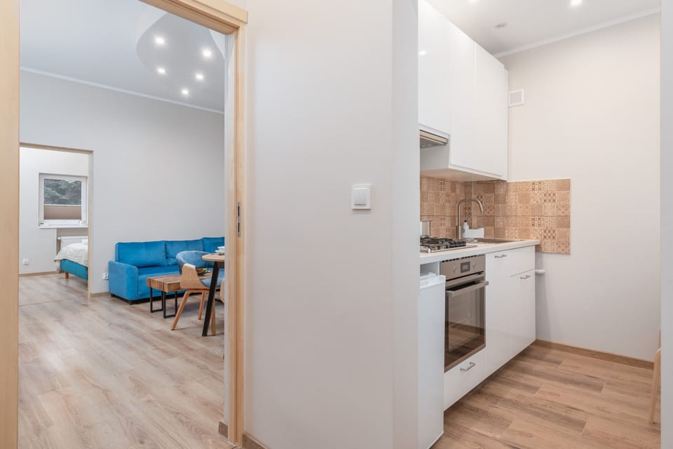 A bright kitchen with wooden flooring, white cabinets, and a view into the dining area.

