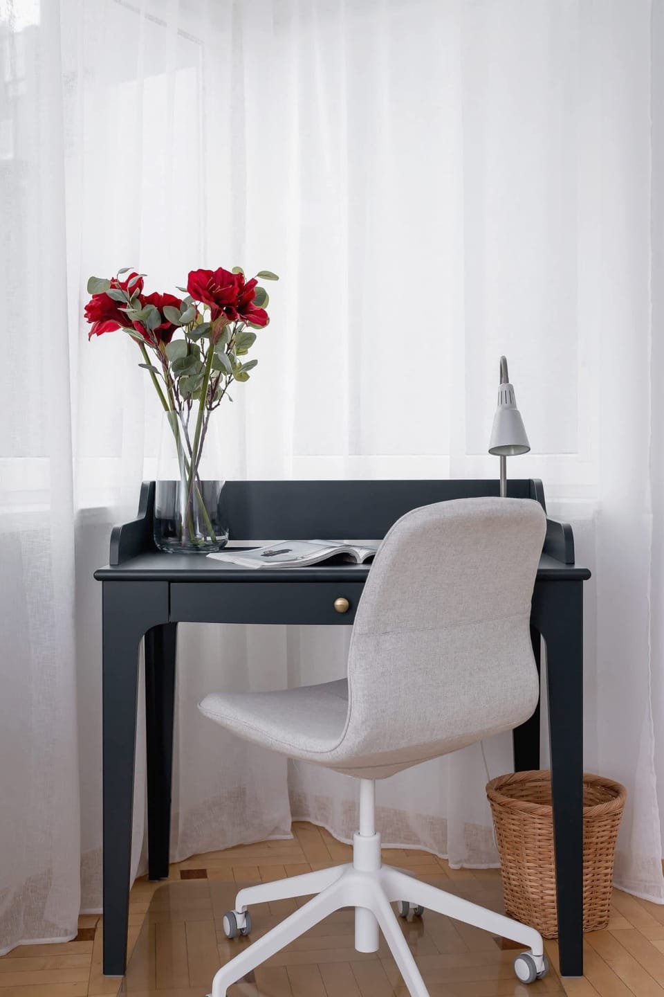 A small work desk by the window with a modern chair and fresh flowers.
