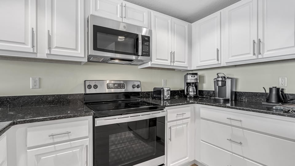 White cabinetry and black granite countertops surround stainless steel appliances in the kitchen corner.