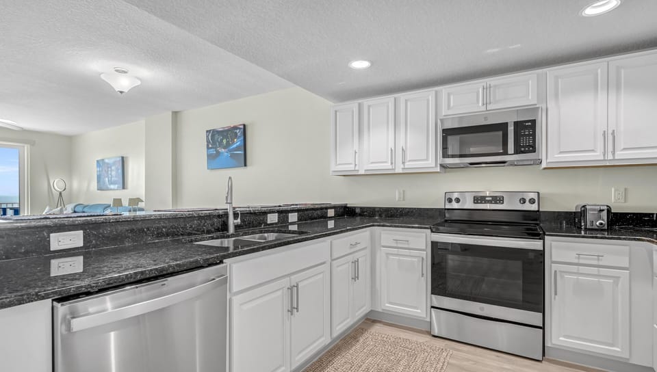 White cabinetry surrounds stainless steel appliances in the kitchen, featuring black granite countertops and a double sink.