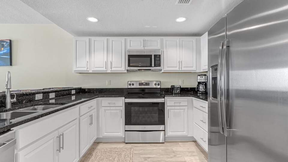 U-shaped kitchen with white cabinetry, black granite countertops, stainless steel appliances, and recessed lighting.