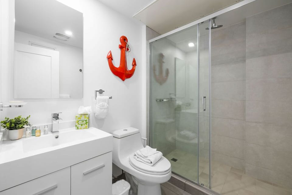 Your private bathroom features a sleek glass-enclosed shower and crisp white vanity, complete with all the essentials and a cheerful coastal touch.