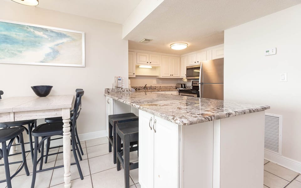 This kitchen features sleek stainless appliances, granite countertops, and a cozy dining area with stylish black chairs