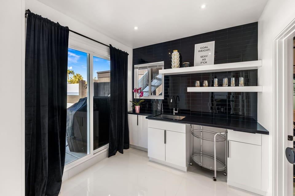Kitchenette with glossy black subway tile, sink, open shelving, bar cart, and sliding door to the patio