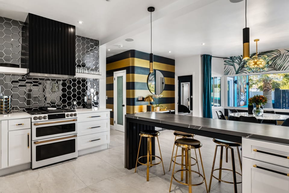Designer kitchen with double oven range, black hex-tile backsplash, dark marble island, and gold bar stools for four
