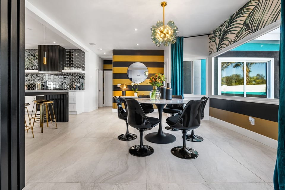 Dining area - tulip table with black molded chairs, gold bubble chandelier, bold black-and-gold striped accent wall, open to kitchen