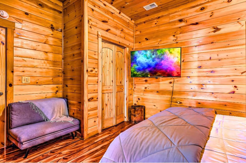 Cozy bedroom corner with a plush loveseat, wood paneling, and a TV for comfort!