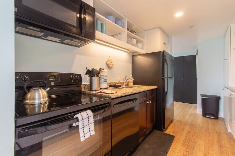Enjoy the convenience and elegance of this well-equipped kitchen. With modern black appliances, granite countertops, and open shelving, every meal preparation will be a breeze. A perfect space for culinary adventures!