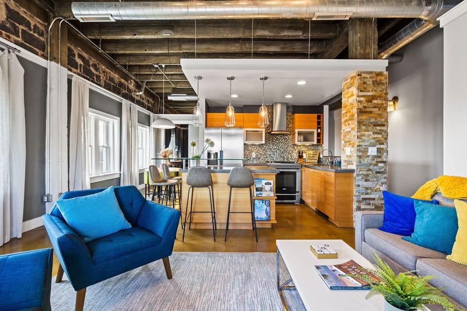 Open-concept kitchen flows seamlessly into the living area, featuring exposed brick, industrial ceilings, and modern finishes throughout.