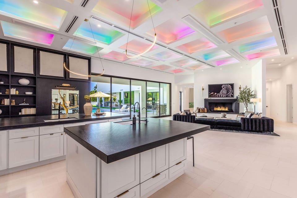 The open-concept kitchen shines with a massive island, sleek cabinetry, modern lighting, and colorful ceiling accents that bring energy into the space.