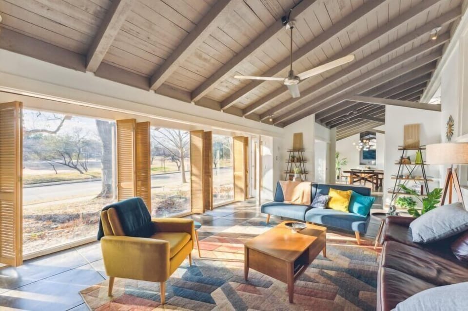 Super Cozy living Room with floor to ceiling windows, park view, exposed wood vaulted ceilings, concrete tiled floors, and mid-centruy modern decor. 