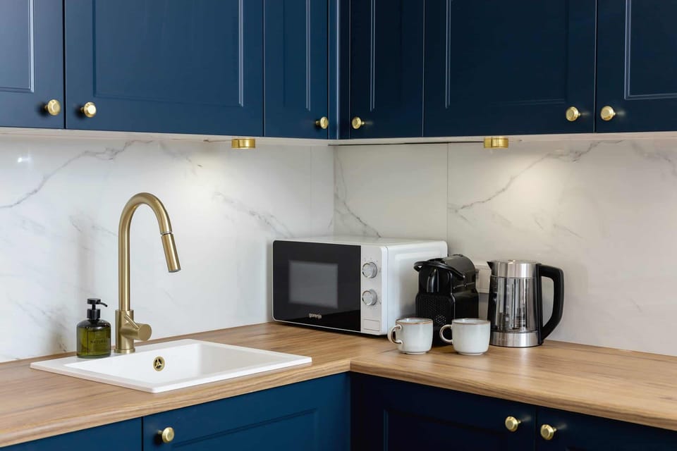A modern kitchen with navy blue cabinets, gold accents, and practical appliances.
