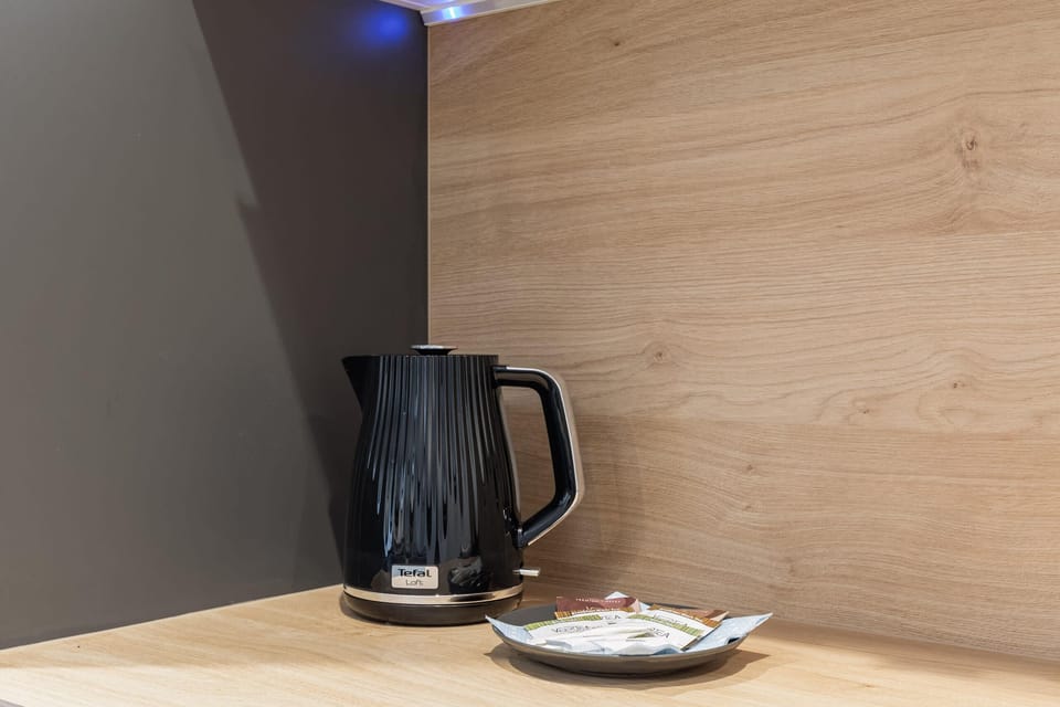 Coffee machine and kettle on a countertop with a natural wood backsplash.
