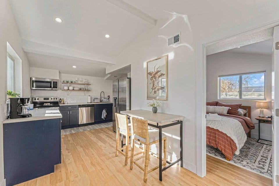 - Bright kitchen features open shelving, stainless appliances, and two seater dining nook
- Natural wood floors and white walls reflect sunlight beautifully across the space
- Thoughtful layout connects to both the bedroom and main living area
