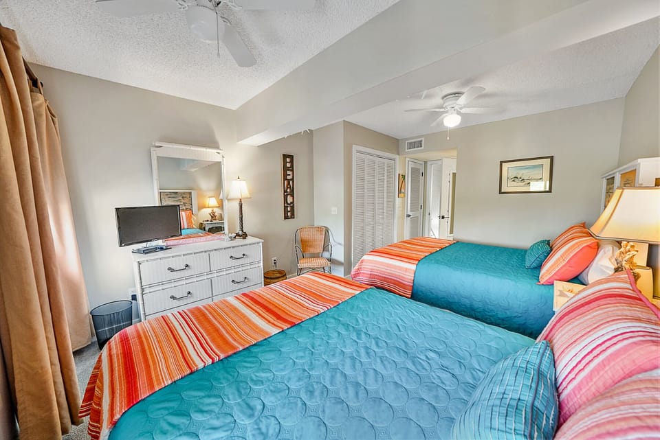 Drift off to peaceful sleep in this bright bedroom featuring twin beds with vibrant tropical bedding and calming coastal touches.