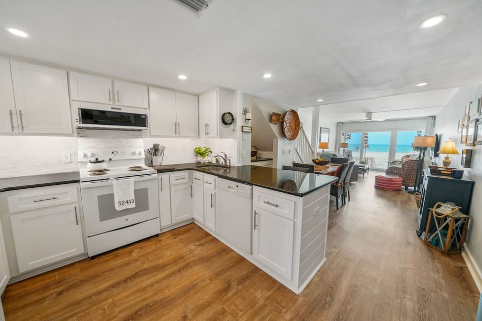 Step into your spacious kitchen featuring crisp white cabinets, sleek granite counters, and gleaming appliances—perfect for preparing beachside meals.