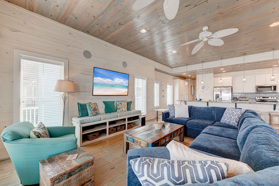 Relax in this coastal living space with plush seating, wood ceilings, and open kitchen where comfort meets beach vibes.