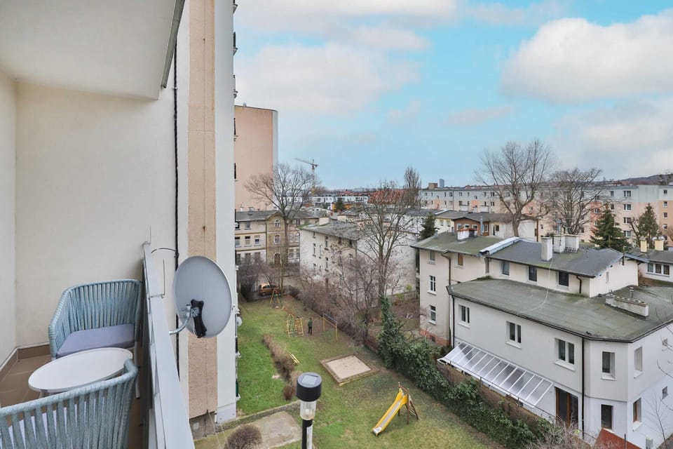 A balcony with seating and a view of nearby houses and greenery.
