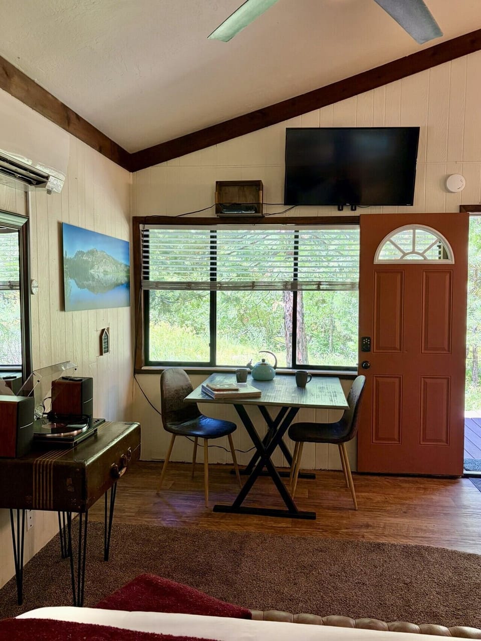 This sitting area combines a table, record player, television, and forest views within the open studio.